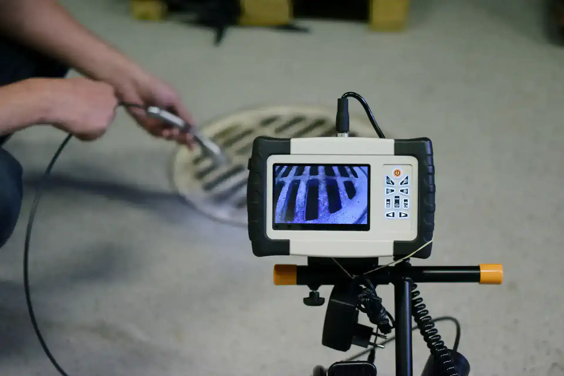 A plumber in Pasco County, FL uses a sewer inspection camera to examine the inside of a drain; the camera&rsquo;s monitor displays the grate pattern of the drain cover.