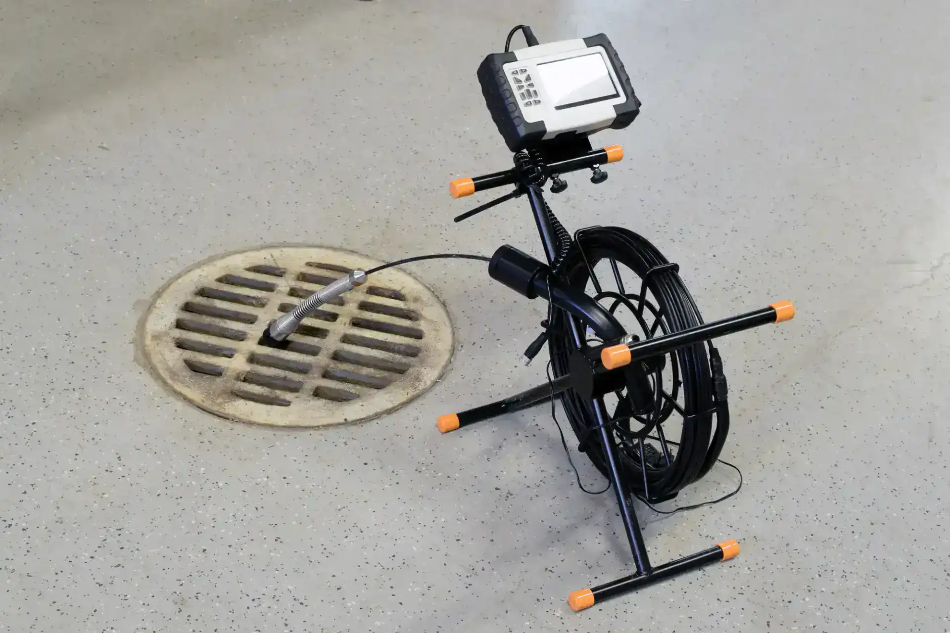 A plumber in Pasco County, FL positions a sewer inspection camera with a coiled cable and monitor next to an open floor drain, preparing for inspection inside a building.